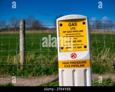 Ein gelbes Warnzeichen, das auf eine Hochdruck-Gasleitung (HP) über Felder in einem ländlichen Gebiet im Nordwesten Großbritanniens hinweist. Stockfoto