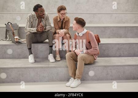 In voller Länge Porträt von drei Studenten chatten während der Pause in der modernen College-Lounge, Copy Space Stockfoto