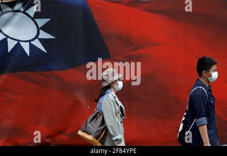 Taipeh, Taiwan. April 2021. Taiwanesen, die eine Gesichtsmaske tragen, gehen an einem riesigen Banner mit einer taiwanesischen Nationalflagge vorbei, inmitten zunehmender Spannungen mit China. Während Peking mehr Düsenjäger auf die Insel schickt, sagte der taiwanesische Außenminister Joseph Wu, dass Taiwan sich „jeden letzten Tag“ verteidigen wird, während es die Beziehungen zu den Vereinigten Staaten in den Bereichen Militär, Wirtschaft, Technologie und medizinische Dienste gefördert hat. Quelle: Daniel Ceng Shou-Yi/ZUMA Wire/Alamy Live News Stockfoto