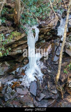 Kleiner gefrorener Wasserfall, der über einen felsigen Felsvorsprung in einem Wald absteigt. Eis hängt in der Luft. Stockfoto