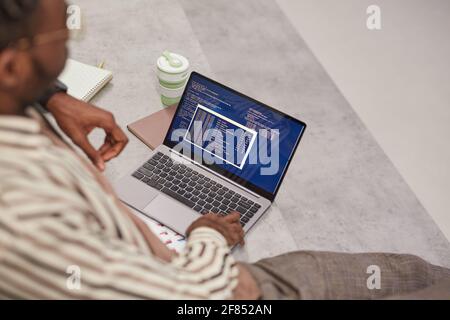 Blick auf den jungen afroamerikanischen Mann mit Laptop und IT-Code auf dem Bildschirm, während er im College studiert oder freiberuflich arbeitet, Kopierraum Stockfoto