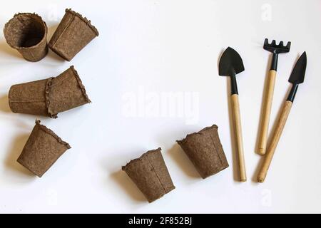 Gartenarbeit zu Hause. Anbau von Lebensmitteln am Fenster. Werkzeuge, Torftöpfe für Sämlinge, Samen. Draufsicht. Flatlay auf weißem Hintergrund Stockfoto