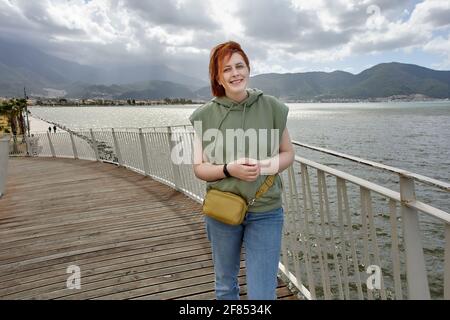 Lächelnde junge europäische Frau in der Nähe des Meeres in Fethiye, Türkei, im frühen Frühjahr. Stockfoto