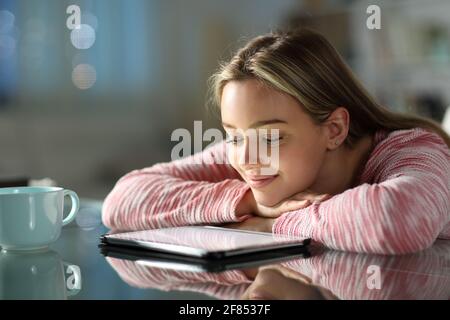 Fröhlicher Teenager, der sich Online-Videos auf einem Tablet auf einem Tisch ansieht In der Nacht zu Hause Stockfoto