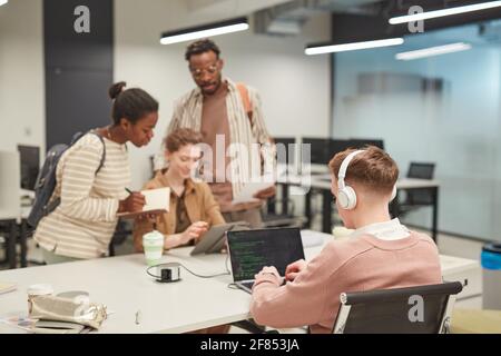 Gruppe von jungen Menschen, die Computer in der Schulbibliothek benutzen, konzentrieren sich auf junge Männer, die Code im Vordergrund schreiben, Kopierraum Stockfoto