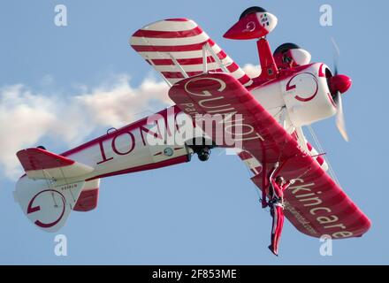 Sarah Tanner, Wing Walker mit Aerosuperbatics Wing Walking Team, das von Guinot hängt, sponserte Boeing Stearman Doppeldecker während des invertierten Stunts. Mutiger Akt Stockfoto