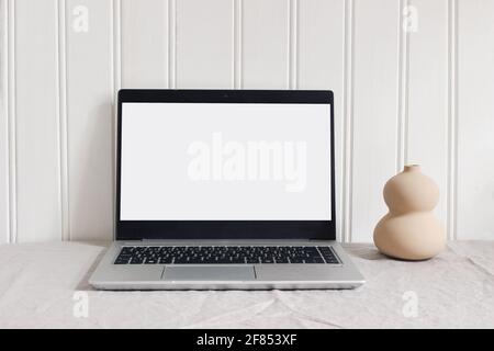 Moderne, minimale Arbeitsplatzzusammenstellung. Notebook-Mock-up-Szene. Vase aus organisch geformter Keramik und Laptop auf beigefarbenem Leinentischtuch im Hintergrund. Weiß Stockfoto