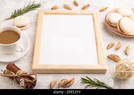 Weißer Holzrahmen-Mockup mit einer Tasse Kaffee, Mandeln und Makronen auf grauem Beton-Hintergrund. Leer, Seitenansicht, Stillleben. Stockfoto