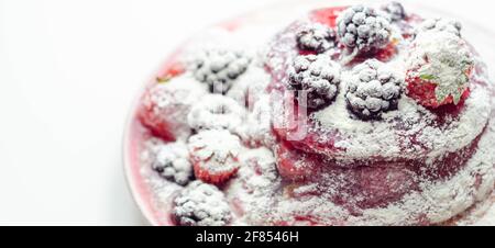 Die Pfannkuchen werden mit Erdbeeren, Blaubeeren und Brombeeren gestapelt, mit Soße gekrönt und mit Puderzucker bestreut, süßes Frühstück Stockfoto