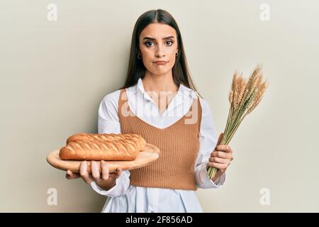 Schöne Brünette junge Frau hält hausgemachtes Brot und Spike Weizen deprimiert und sorgen für Not, Weinen wütend und Angst. Trauriger Ausdruck. Stockfoto