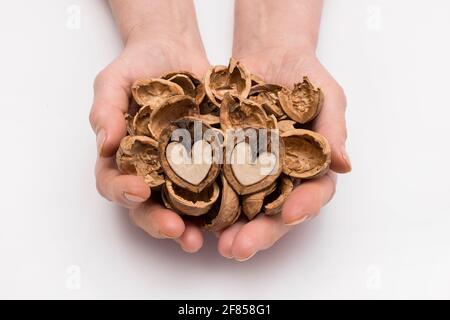 Frau hält ihre Hände mit einem Bund geschälter Schale und zwei Hälften einer Walnuss in Form eines Herzens auf weißem Hintergrund, isoliert. Nut-Konzept. Stockfoto