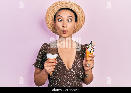 Schöne hispanische Frau mit kurzen Haaren, die Eiszapfen isst, die Fische mit Mund und blinden Augen ins Gesicht machen, verrückt und komisch. Stockfoto