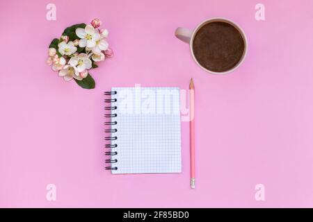 Ein Notizbuch für Notizen liegt auf einem rosa Hintergrund, neben Stift, Kaffee und Blumen. Planung persönlicher Zeit und Arbeiten Stockfoto