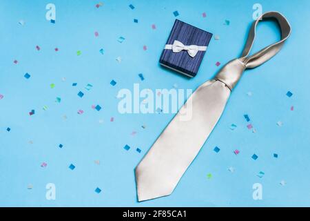 Blaue Geschenkbox mit weißer Krawatte, auf blauem Hintergrund mit farbigem Konfetti. Vatertagskonzept, herzlichen Glückwunsch an einen Mann, Sohn, Kollegen. Stockfoto