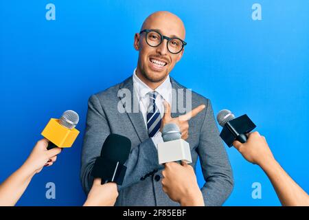Kahlköpfiger Mann mit Bart, der von Reportern mit Mikrofonen interviewt wurde Lächelnd fröhlich zeigend mit Hand und Finger bis zum Seite Stockfoto