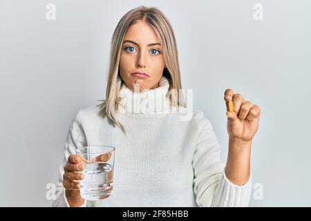 Schöne blonde Frau hält Pille und Glas Wasser deprimiert und sorgen für Not, weinen wütend und Angst. Trauriger Ausdruck. Stockfoto