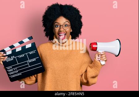 Junge afroamerikanische Frau mit Videofilm-Klapboard und Megaphon feiert verrückt und erstaunt über den Erfolg mit offenen Augen schreiend aufgeregt. Stockfoto
