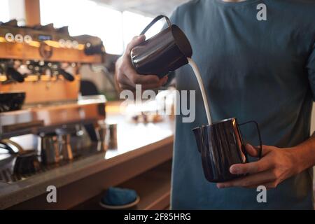 Beschnittenes Porträt eines jungen Barista, der beim Zubereiten von frischem Kaffee im Café oder Café in Latte Rahm eingießt, Kopierbereich Stockfoto