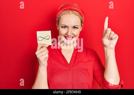 Junge blonde Frau hält unendliche Symbol Erinnerung überrascht mit einer Idee oder Frage Zeigefinger mit glücklichem Gesicht, Nummer eins Stockfoto