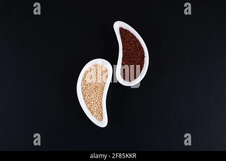 Rote und weiße Quinoa-Samen in weißen Schalen auf schwarzem Hintergrund. Glutenfreies altes Getreide. Gesunde Ernährung. Stockfoto