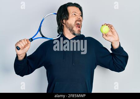 Kaukasischer Mann mittleren Alters spielt Tennis mit Schläger und Ball wütend und wütend schreiend frustriert und wütend, schreiend vor Wut. Wut und Aggression Stockfoto