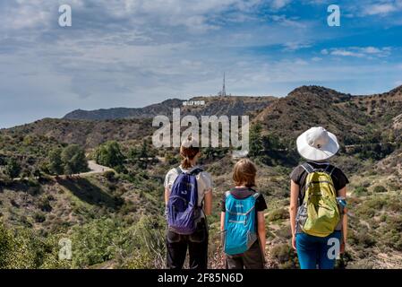 Drei Kinder blicken von einem Wanderweg im Griffith Park, Los Angeles, Kalifornien, auf das Hollywood-Schild, während sie in einem Familienurlaub wandern.
