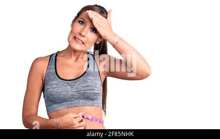 Junge schöne hispanische Frau trägt Sportkleidung mit Maßband gestresst und frustriert mit Hand auf dem Kopf, überrascht und wütend Gesicht Stockfoto