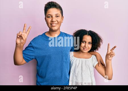 Junge hispanische Familie von Bruder und Schwester in legerer Kleidung zusammen lächelnd Blick auf die Kamera zeigt die Finger tun Siegeszeichen Stockfoto