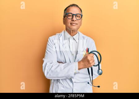 indischer Mann mittleren Alters mit Doktor Mantel hält Stethoskop entspannt mit ernstem Ausdruck auf dem Gesicht. Einfach und natürlich Blick auf die Kamera. Stockfoto
