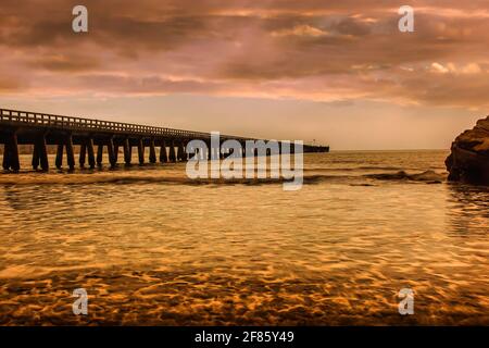 Rote Wolkenlandschaft spiegelte sich am Meer in der Tolaga Bay daneben wider Der historische Wahrzeichen Pier Stockfoto