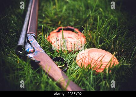 Eine fallgehärtete Tristar Bristol 28ga nebeneinander im Gras ruht neben einem Paar orangefarbener Tonziele. Eines der tonhaltigen Ziele ist gebrochen Stockfoto