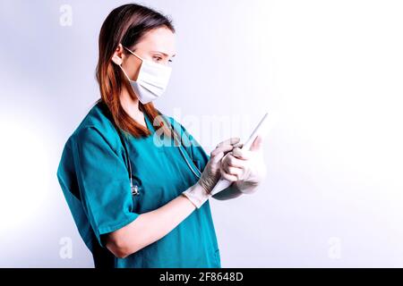 Seitenansicht der Ärztin des Krankenhauses mit Gesichtsmaske Stethoskop und Tablet, die einen Bericht überprüft. Medizin- und Technologiekonzept auf weißem Hintergrund Stockfoto