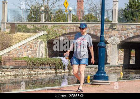 Frederick, MD, USA 04-07-2021: Eine kaukasische Frau mittleren Alters in legerer Sommerkleidung geht allein im Carroll Creek Park in der Innenstadt von Frederi Stockfoto