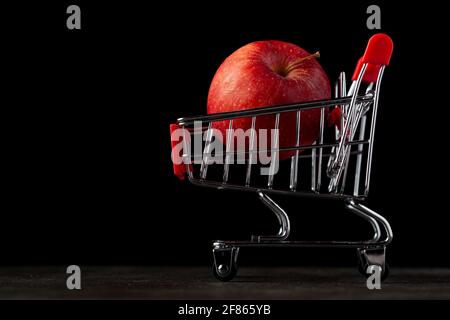 Dunkles Hintergrundbild mit einem Spielzeug-Warenkorb gefüllt mit Ein roter Apfel EIN Konzept für den Kauf gesünder Obst und Gemüse im Lebensmittelgeschäft oder sup Stockfoto