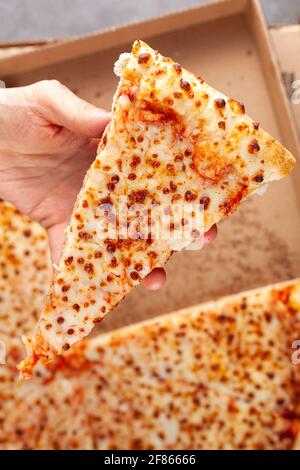 Nahaufnahme von oben, Bild einer kaukasischen Frau, die im Hintergrund eine Scheibe Frischkäse-Pizza mit einer großen Pizza in einer Kartonbox hält. Konzeptbild für Stockfoto