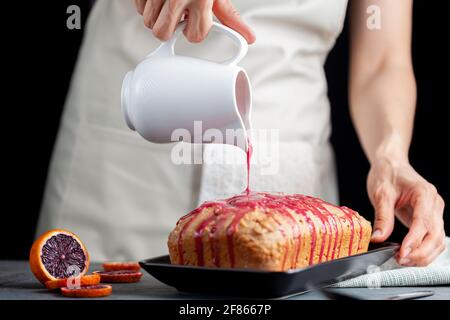 Nahaufnahme Bild von frischen hausgemachten Blut-Orange-Kuchen in einer Laib-Pfanne gemacht und serviert auf schwarzem Porzellan-Teller auf dunklem Stein Hintergrund. Eine Frau ergießt sich Stockfoto