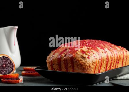 Nahaufnahme Bild von frischen hausgemachten Blut-Orange-Kuchen in einer Laib-Pfanne gemacht und serviert auf schwarzem Porzellan-Teller auf dunklem Stein Hintergrund. Es hat Blutorang Stockfoto