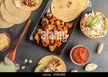 Nahaufnahme eines mexikanischen Taco-Tellers mit Maistortillas, vorgekochten Hühnerstücken, Kohlschlaw, geschreddertem Käse, Salsa und Rahmsoße Stockfoto