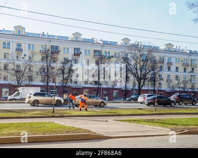 Moskau. Russland. 06. April 2021. Orangefarbene uniformierte Hausmeister, die auf einer Straße in der Stadt den Rasen fegen. Sonniger Frühlingstag. Die Arbeit der Gemeinde Stockfoto