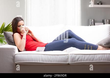 Trendy Casual junge Frau auf einem Sofa entspannen trinken ein Tasse Kaffee in voller Länge Seitenansicht Stockfoto