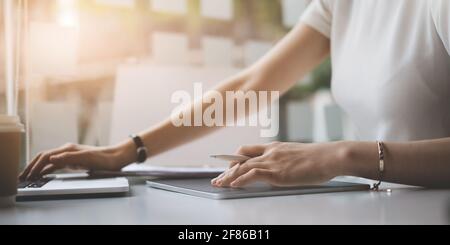 Modedesignerin hält Stylus Pen und verwendet ein digitales Tablet und zeichnet Skizzen von menschlichen Figuren, während sie am Holzschreibtisch im Heimbüro arbeitet. Stockfoto