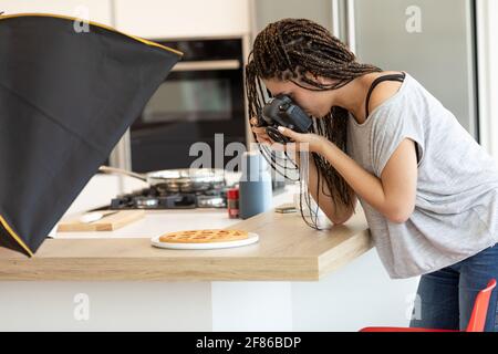 Junge Fotografin fotografiert Essen in der Küche und lehnt sich darüber Eine frisch gebackene Tarte mit ihrer Kamera in der Nähe Ansicht von oben Stockfoto