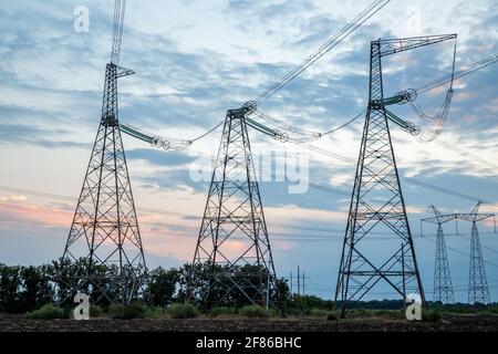 Elektrische Masten und Hochspannungsleitungen im Hintergrund bei Sonnenuntergang. Gruppieren Sie die Silhouette der Sendetürme. Stockfoto