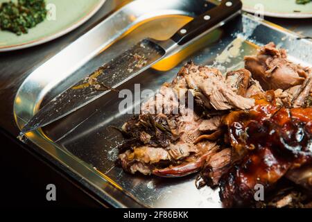 Gebackenes, saftiges Fleisch, in Stücke geschnitten, liegt auf einem Metalltablett und daneben befindet sich ein Küchenmesser. Stockfoto