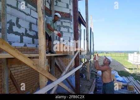 Ein Arbeiter wirft Ziegel auf einen anderen Arbeiter, Bauarbeiten in einem privaten Bereich, Holzgerüst in der Nähe der Wände.neu Stockfoto