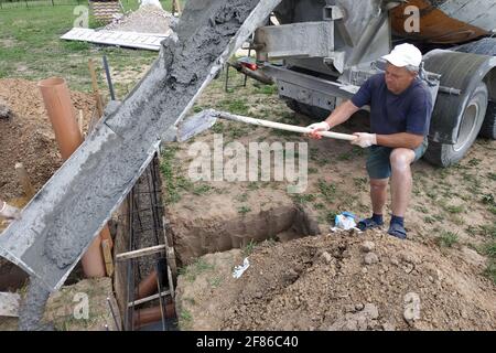 Gießen von Zement in den Graben mit einem Mischer, Bauarbeiten im Sommer.neu Stockfoto