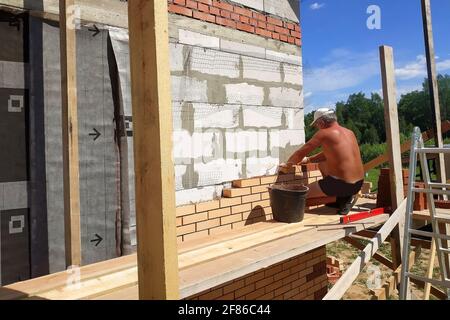Der Meister stellt das Mauerwerk aus dem vorderen Ziegel, die Erwärmung des Hauses draußen, die Bauarbeiten im Sommer.neu Stockfoto