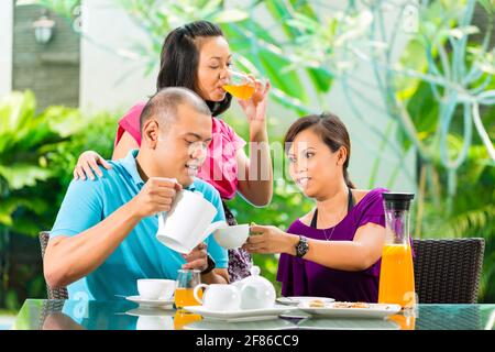 Asiatischen Freunden Kaffee auf der Veranda vor dem Haus, im Hintergrund ein tropischer Garten Stockfoto