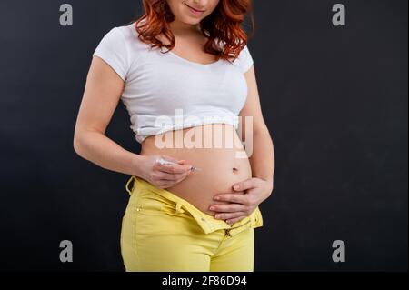 Eine gesichtslose Schwangerin spritzt ihr Insulin in den Magen. Zukünftige Mutter. Subkutane Verabreichung eines hormonellen Medikaments. Gesundheitswesen. Stockfoto