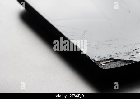 Nahaufnahme eines defekten Smartphones mit gesprungenem Bildschirm auf grauem Hintergrund isoliert. Stockfoto